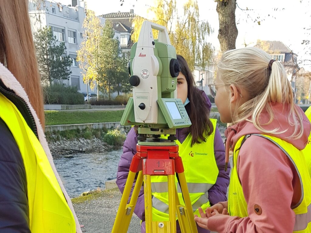 Schülerinnen schauen anlässlich des Zukunftstages durch ein Vermessungerät. Sie befinden sich an der Glatt.